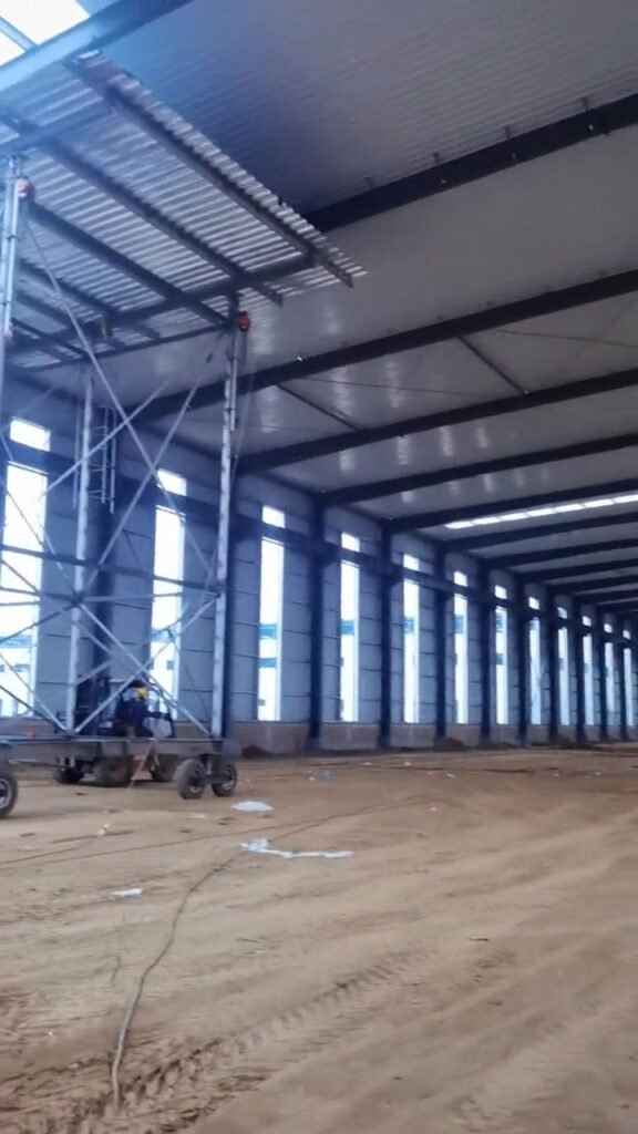 Operarios instalando aislamiento térmico de lana de vidrio de 10cm en el techo de naves metálicas prefabricadas.
