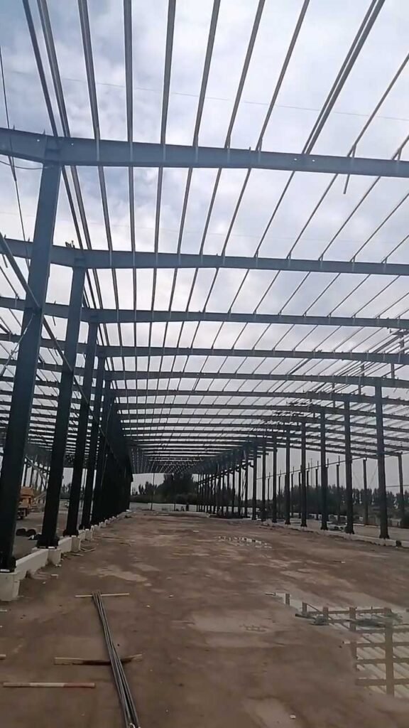 Wide clear-span interior of a commercial steel warehouse manufactured by a China steel building exporter, displaying heavy-duty painted primary columns.