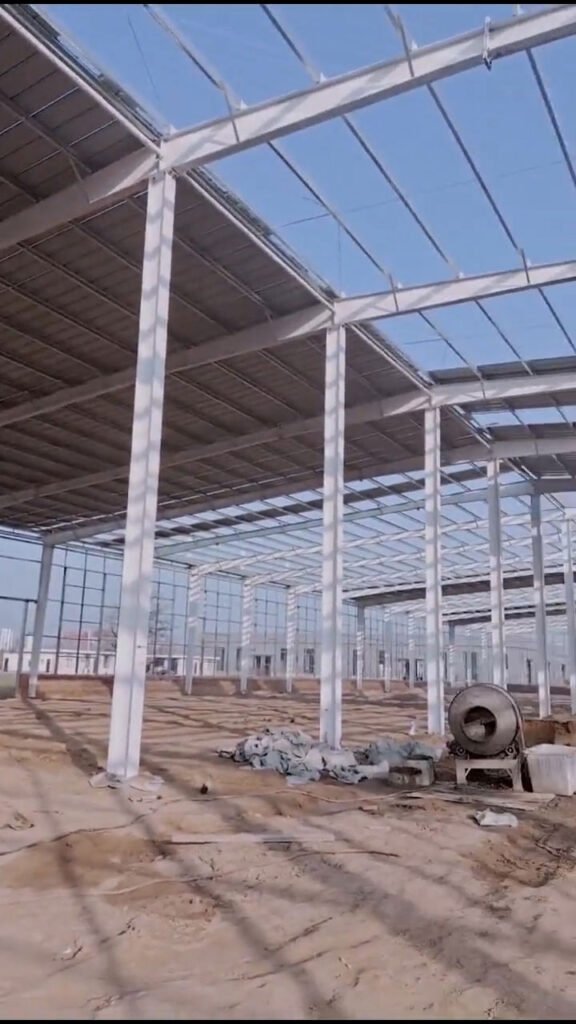 Interior view of a multi-span complete steel building package featuring Q355 high-strength painted steel columns and a perfectly leveled foundation interface.
