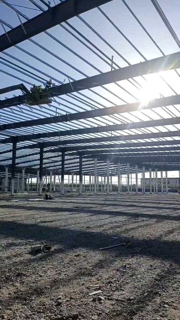 Sunlight illuminating the massive steel framework of an industrial warehouse, showcasing the dimensional accuracy of custom steel fabrication services.