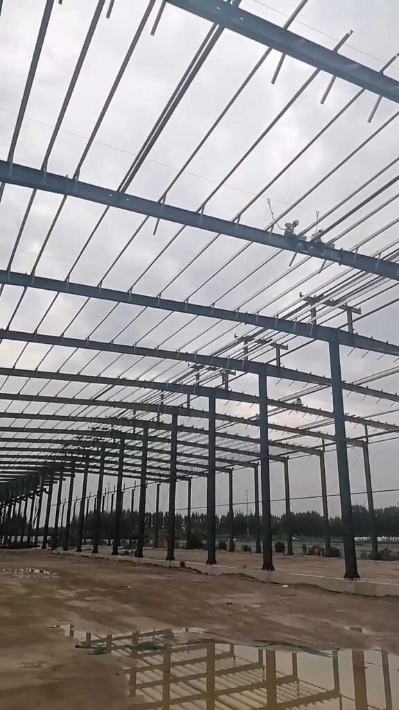 Workers installing galvanized roof purlins on a heavy industrial steel building engineered by a top FOB steel structure supplier in China.