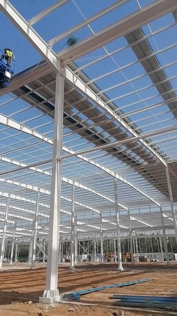 Close-up of workers securing roof framing and tie rods, components that directly dictate the steel consumption calculated in an industrial warehouse quotation.