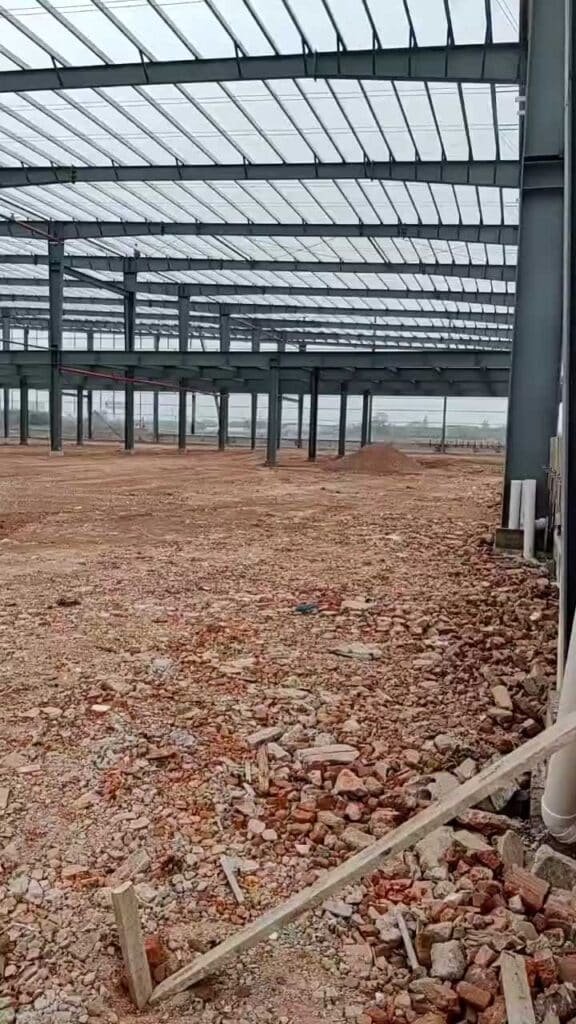 Wide view of a multi-span steel frame warehouse under construction, showing primary steel columns installed on a prepared foundation for a large-scale industrial logistics center.