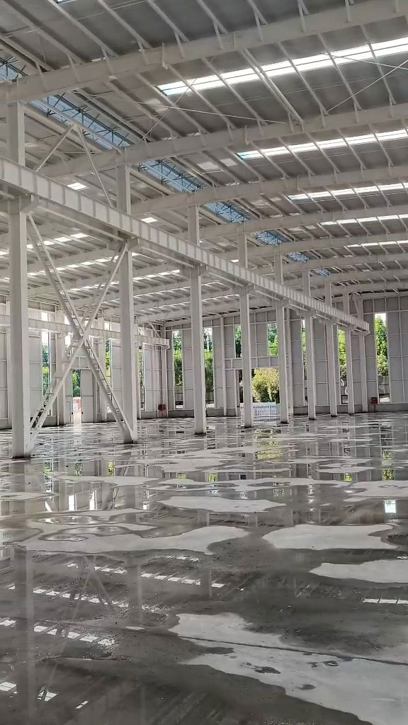 Freshly poured concrete floor reflecting the clean, heavily braced framing of an OEM prefabricated steel building ready for exterior wall panel installation.