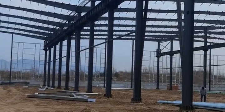 Heavy-duty painted Q355 steel columns securely anchored to concrete foundation pedestals in a commercial steel warehouse factory expansion project.