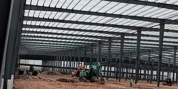 Heavy excavation machinery performing interior ground leveling within a newly erected portal frame warehouse prior to pouring the industrial reinforced concrete slab.