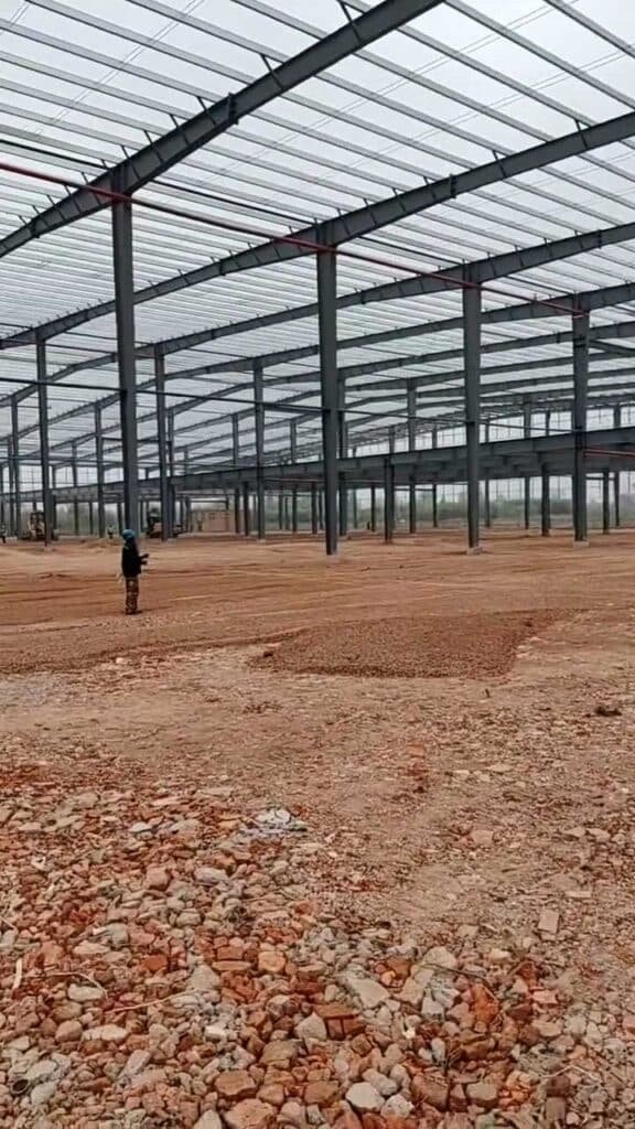 Construction engineer overseeing the erection phase of a massive prefabricated steel frame warehouse, highlighting the precise grid layout of the structural framework.