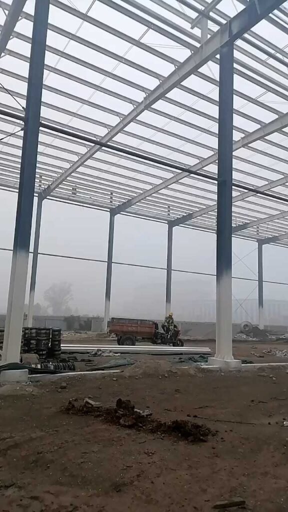 A worker navigating the construction site of an industrial steel building, highlighting the heavy materials and scale that dictate the final steel building price per square meter.