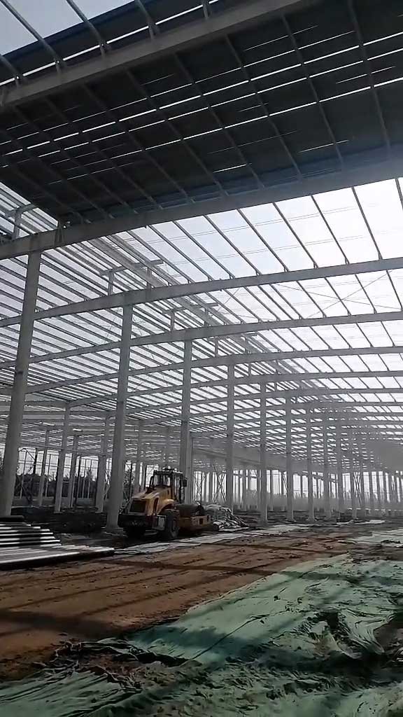 Heavy machinery operating inside a wide-span industrial facility, demonstrating the large-scale manufacturing capacity provided by a reliable steel building wholesale supplier.