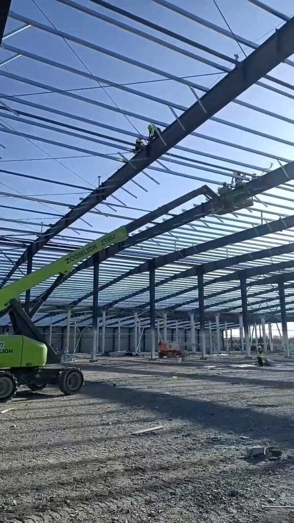 Workers operating a Zoomlion ZT20J telescopic boom lift to assemble precision-engineered roof beams exported by a leading steel fabrication factory.