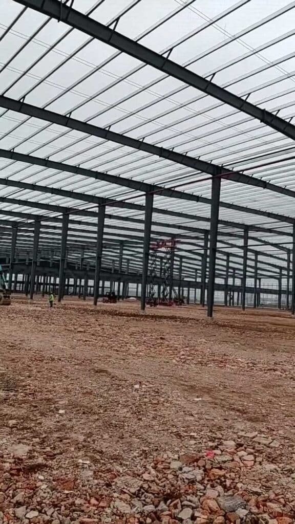 Aerial scissor lifts being utilized to align primary moment connections and install secondary bracing inside a heavy-duty steel frame industrial warehouse.
