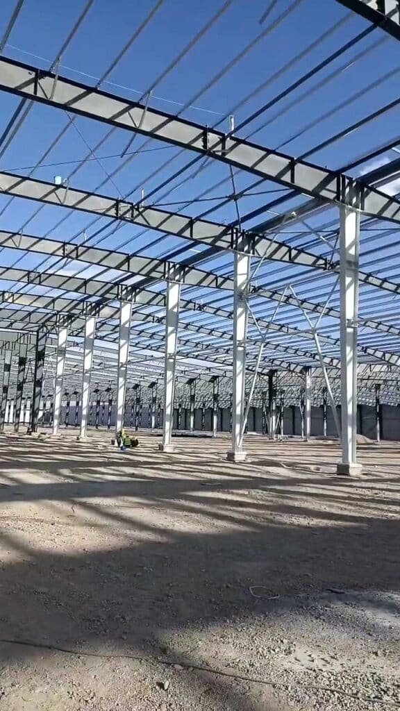 Wide interior perspective from a steel warehouse contractor showcasing perfectly aligned, painted steel columns and a secure foundation interface ready for concrete slab pouring.