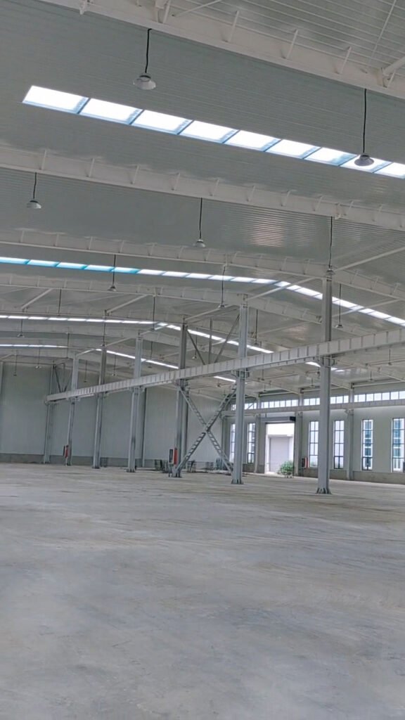 Clean interior view of a wide-span facility manufactured by our steel warehouse direct factory, featuring robust Q355 steel columns and heavy-duty crane support brackets.
