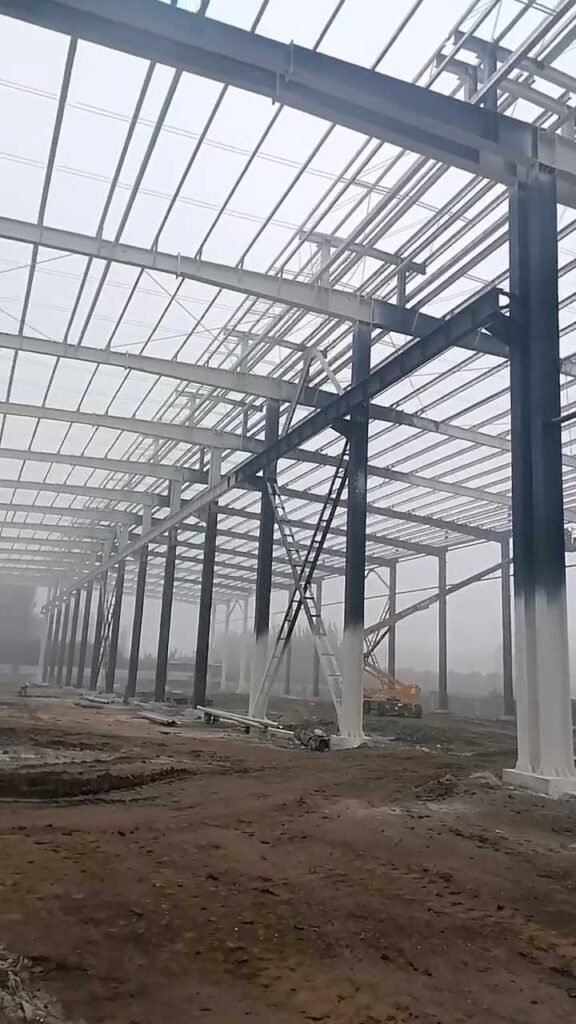 A scissor lift positioned under massive steel roof trusses, demonstrating the specialized installation labor factored into the overall steel warehouse price per m2.