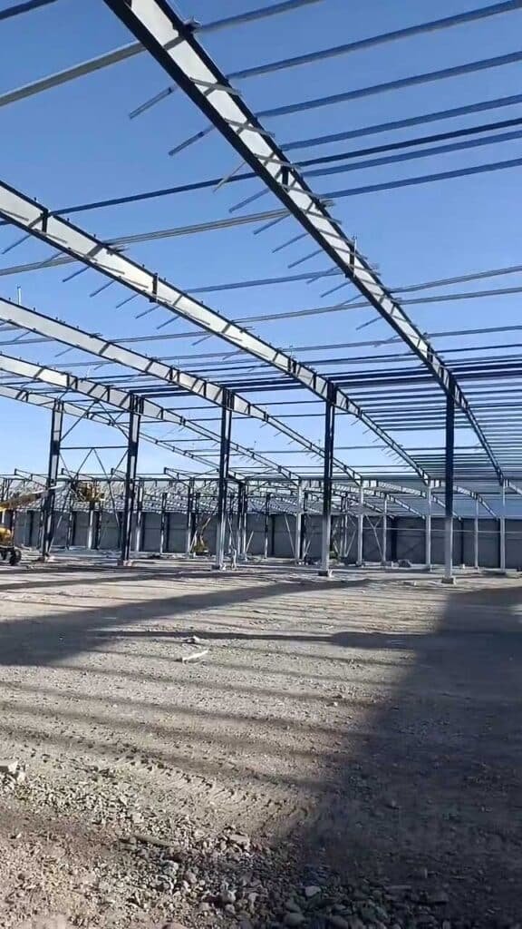 Erection phase showing heavy steel girders and purlins manufactured through precision structural steel fabrication, utilizing heavy lifting equipment on site.