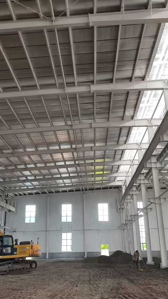 Heavy earthmoving equipment operating safely within the expansive clear span of a warehouse building during the internal concrete slab preparation phase.