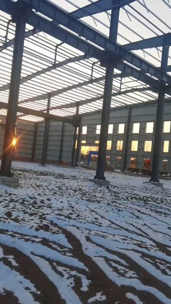 Erection of a steel structure warehouse during winter conditions, demonstrating the weather-independent assembly of bolted steel connections.