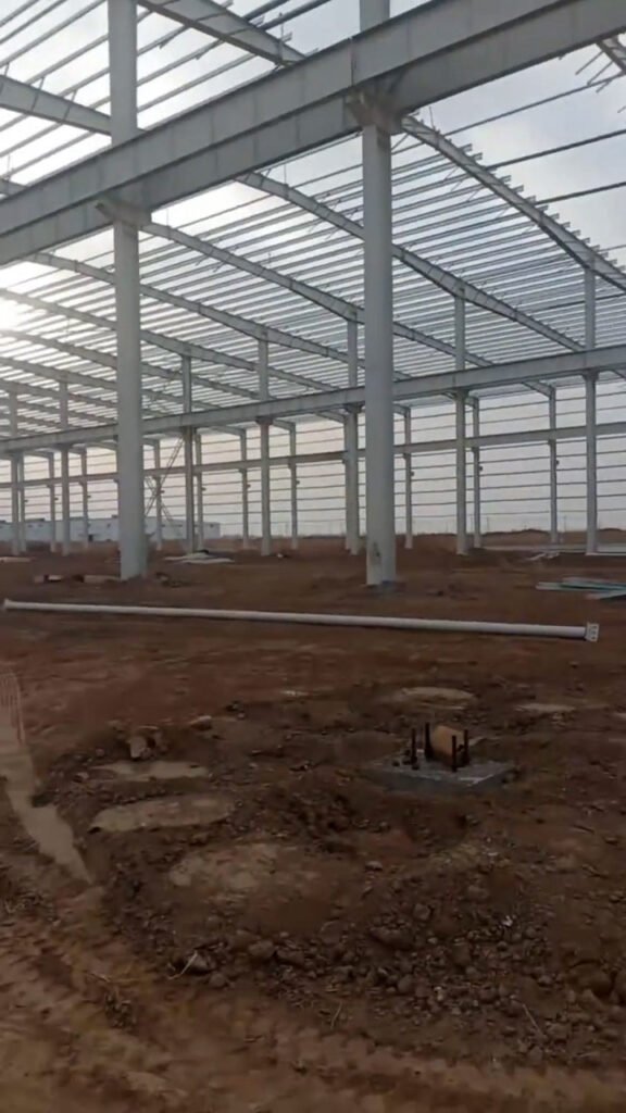 Detalle de cimentación con pernos de anclaje y columnas de acero montadas en almacén con estructura metálica.