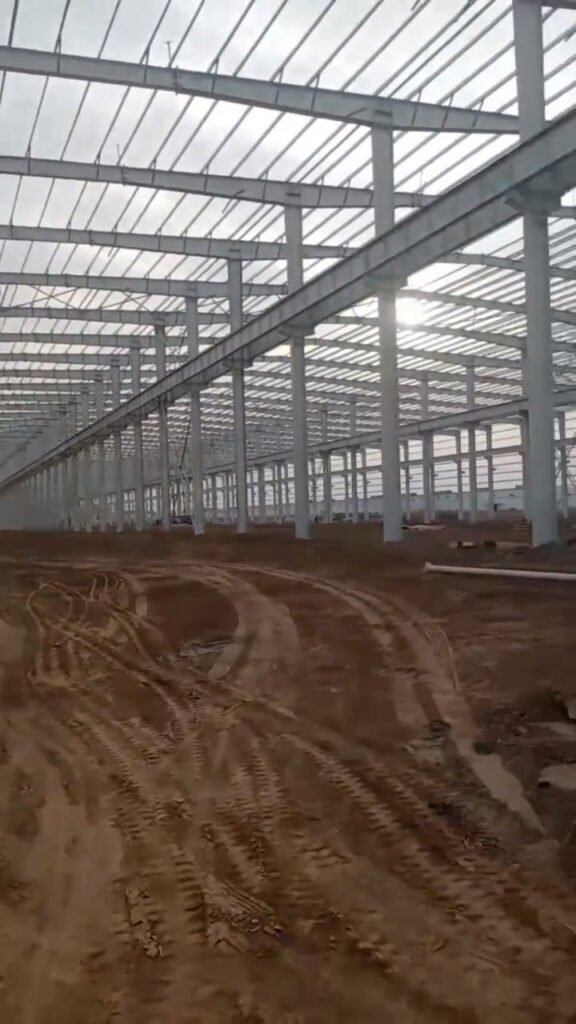 Perspectiva de columnas de acero, vigas carrileras para puente grúa y arriostramientos en un almacén con estructura metálica.