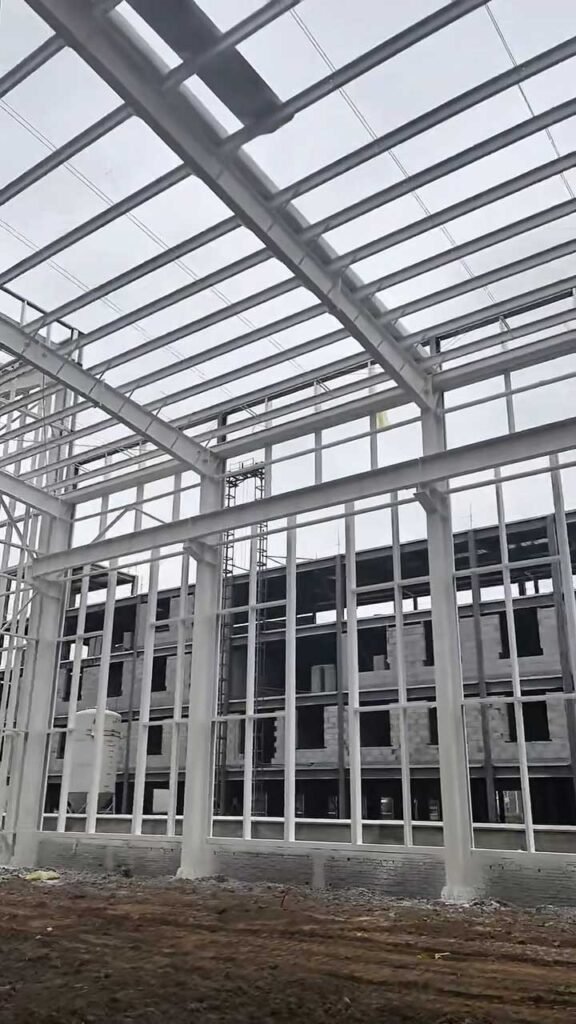 Vista frontal de pórticos rígidos y arriostramientos de cubierta de un edificio prefabricado de estructura metálica en proceso de ensamblaje.