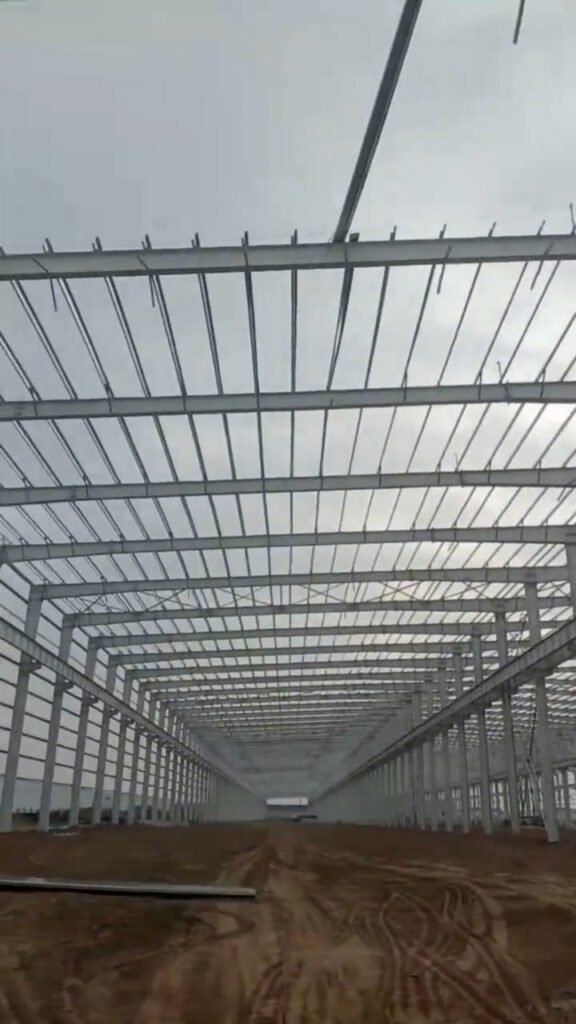 Vista central del pasillo operativo y entramado de cubierta en estructura metálica prefabricada para logística.