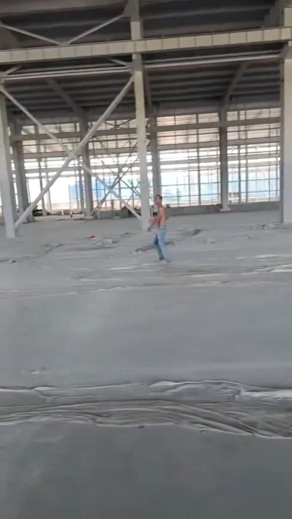 Trabajador supervisando el suelo de cimentación bajo la estructura metálica de una nave industrial.