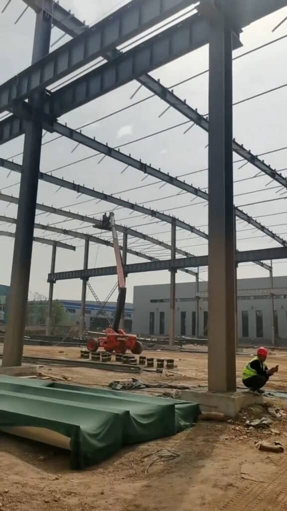 Operario supervisando la construcción de un almacén de acero durante la alineación de vigas y pórticos principales.