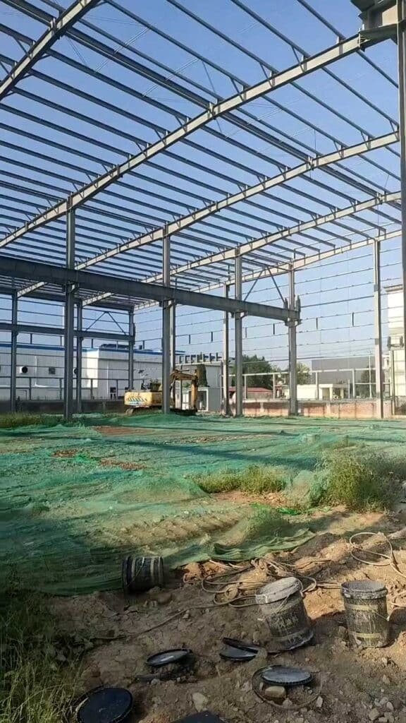 Terreno en preparación bajo la cubierta estructural de una bodega metálica en construcción.