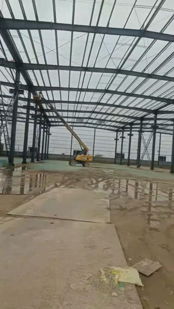 Avance de instalación de columnas de acero en bodega metálica con plataforma elevadora.