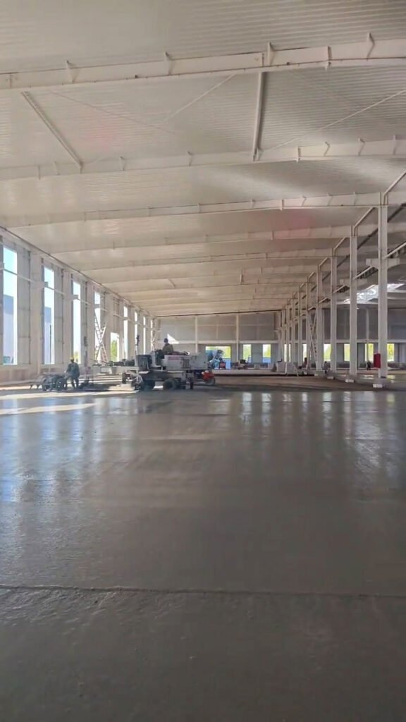 Broad internal perspective of a steel warehouse building with smooth finished concrete flooring.