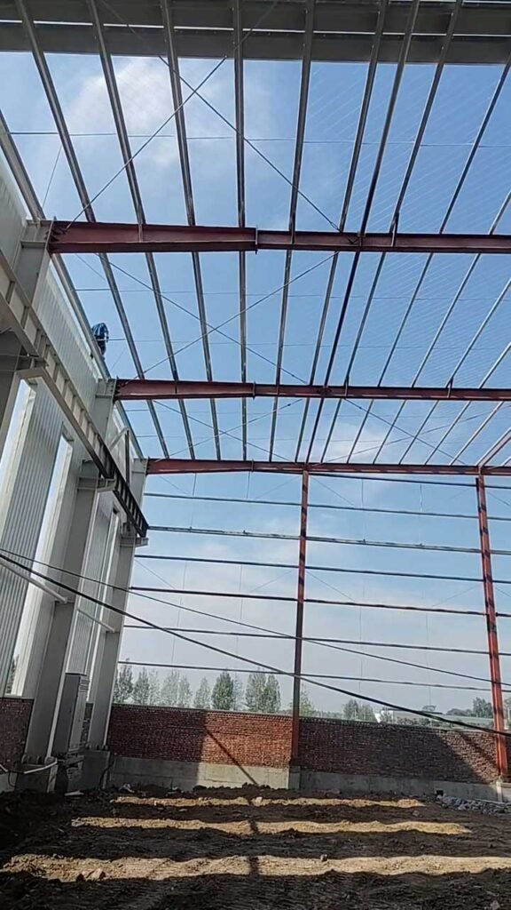 Columnas y vigas de acero pintado en el interior de una nave industrial con cubierta aislante y franjas de iluminación natural