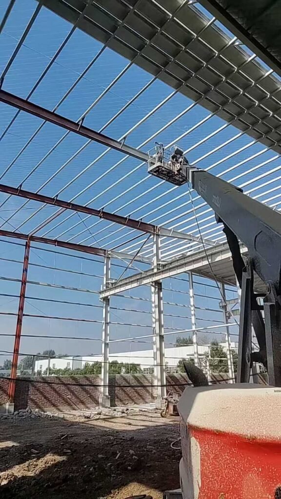 Estructura metálica de una nave industrial con cubierta translúcida, correas de acero y plataforma elevadora durante la instalación del techo.