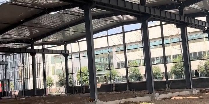 Columnas y vigas de acero de un galpón industrial en construcción junto a una fachada acristalada.