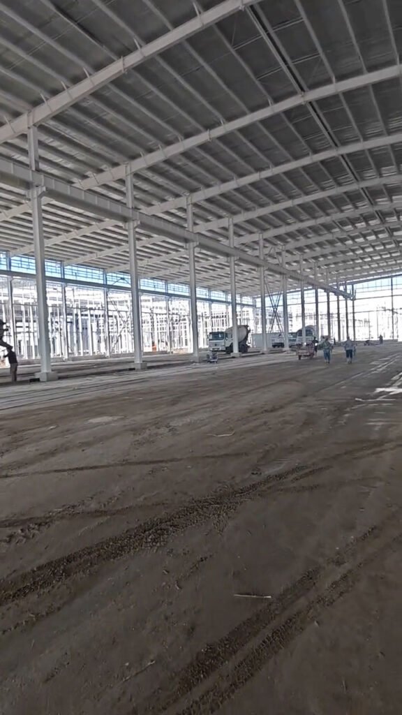 Interior amplio de galpón metálico con pórticos de acero y suelo preparado para concreto.