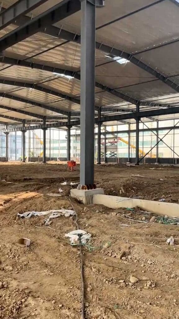 Base de columna de acero apoyada sobre una cimentación de hormigón en un galpón prefabricado en construcción.