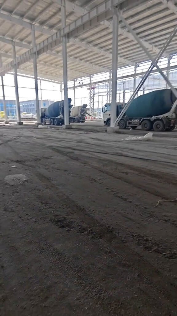 Camiones hormigoneros trabajando en el suelo de concreto de una nave industrial prefabricada