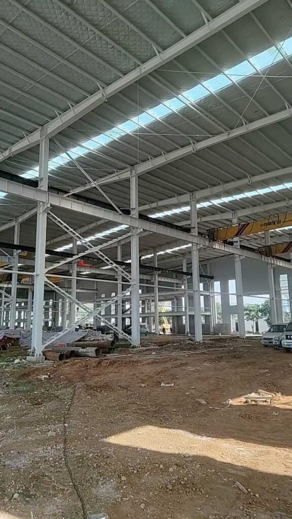 Interior de una nave industrial con estructura de acero, paneles aislantes de cubierta y franjas longitudinales de iluminación natural