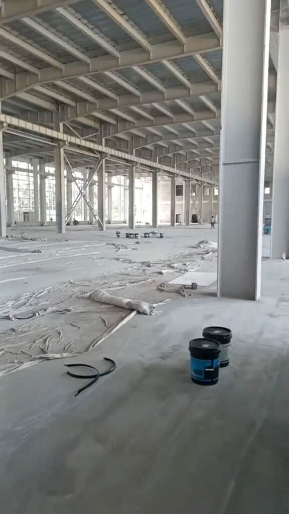 Baldes de pintura anticorrosiva en primer plano durante la construcción de un galpón metálico prefabricado.