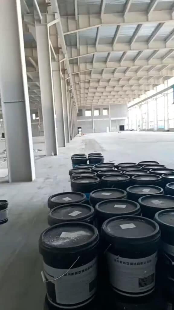 Hileras de baldes de recubrimiento industrial alineados junto a las columnas de un galpón industrial en fase de acabados.